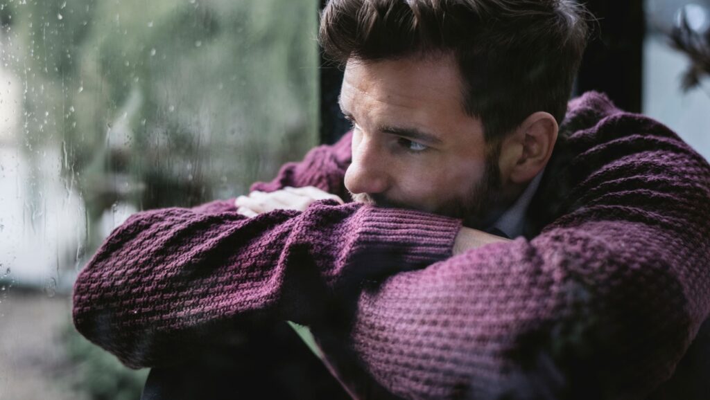 A man with major depressive disorder looks out a rainy window.