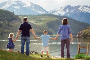 Family holding hands while overlooking a lake and mountains, symbolizing hope through rehab near Fort Lupton, CO at Flatirons Recovery Center.
